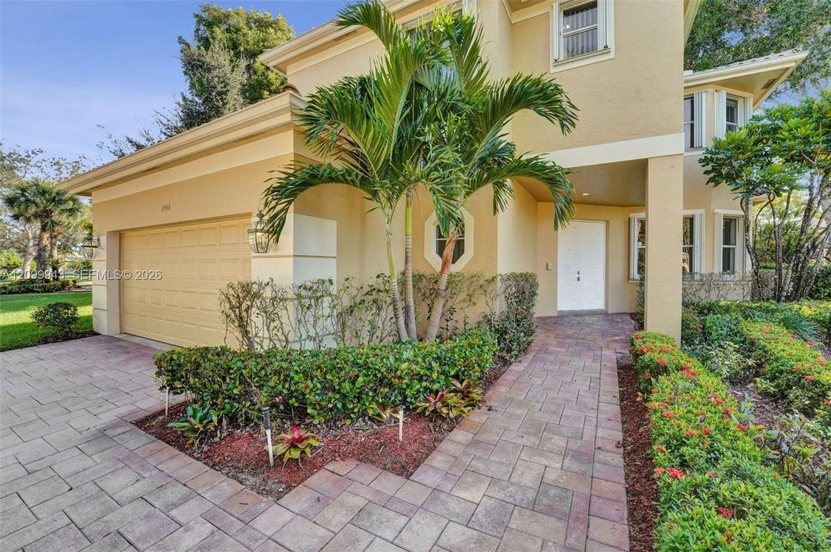 Two-story residence featuring a stucco exterior, paver driveway and walkway, attached garage, and mature palm tree landscaping