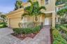 Two-story residence featuring a stucco exterior, paver driveway and walkway, attached garage, and mature palm tree landscaping