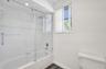 Bathroom featuring a tub-shower combination with frameless glass sliding doors, polished chrome fixtures, square wall tiling, and wood-finish flooring