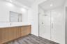 Floating wood-finish vanity with a white countertop and rectangular sink, frameless glass-enclosed shower, polished chrome fixtures, and wood-finish f