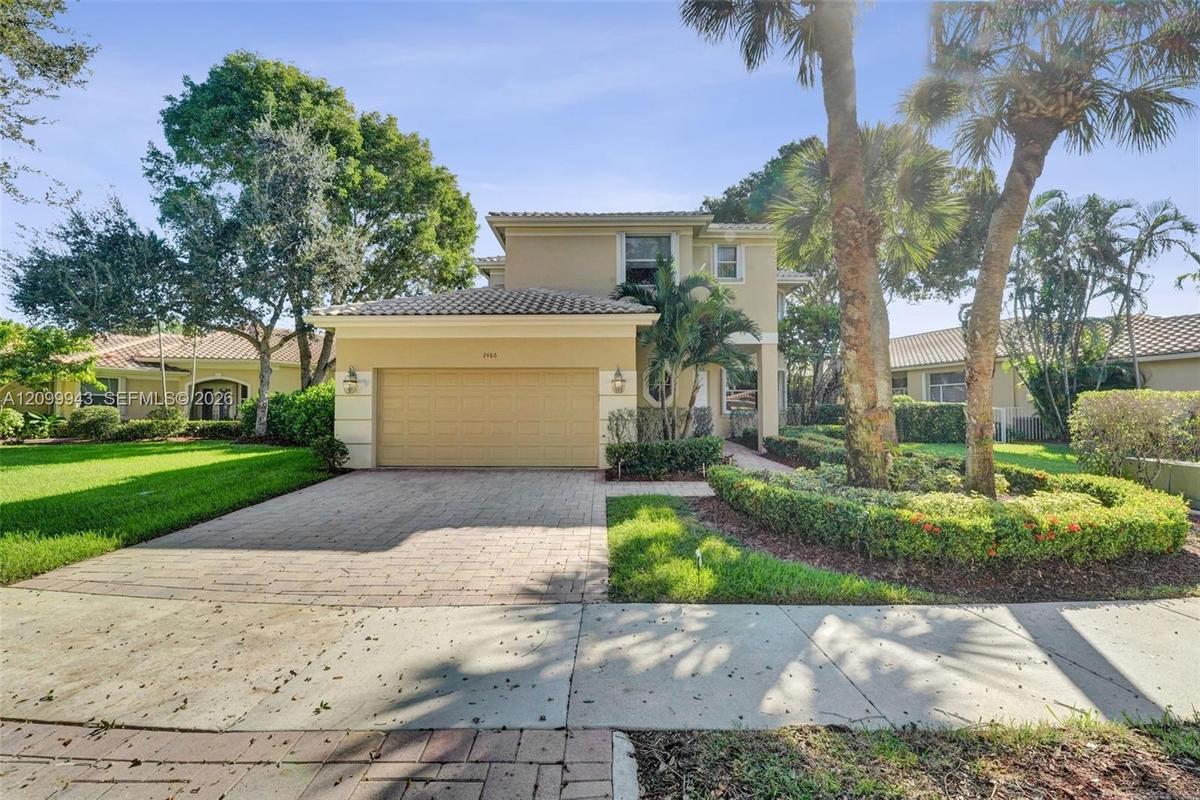 Stucco exterior with a tiled roof, paver driveway, two-car garage, and established landscaping