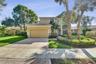 Stucco exterior with a tiled roof, paver driveway, two-car garage, and established landscaping