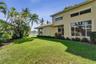 Stucco exterior with multi-level windows, expansive manicured lawn, established palm trees, and professional landscaping