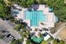 Aerial view of an outdoor swimming pool featuring lap lanes, an integrated spa, paved pool deck, and shaded structures, surrounded by mature landscapi