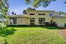 Two-story stucco exterior featuring a tile roof, expansive manicured lawn, multi-pane windows, and privacy fencing