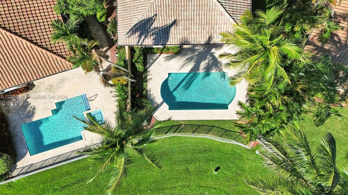 Aerial perspective featuring two outdoor swimming pools, paver decking, lush perimeter landscaping, and tile roofing