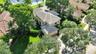 Aerial perspective of a multi-story residence featuring a tile roof, paved driveway, mature trees, and landscaped grounds