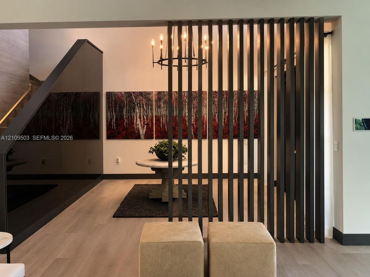 Vertical slatted room divider, wood-finish flooring, high-gloss paneled accent wall, and multi-arm chandelier