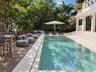Rectangular swimming pool with stone surround, wood-finish decking, and tiered patio steps leading to a white exterior structure