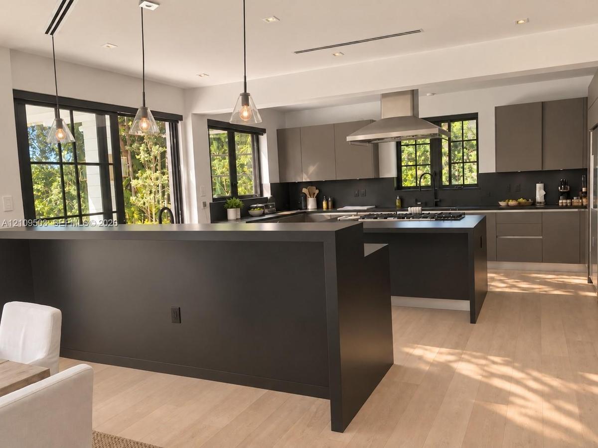 Kitchen featuring matte dark cabinetry, wood-finish flooring, a stainless steel range hood, glass pendant lighting, and a kitchen island with a dark c