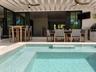 Covered patio featuring an integrated outdoor kitchen, multi-panel retractable glass doors, dual ceiling fans, and an inground swimming pool with ston