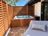 Private outdoor area featuring a built-in jetted spa, wood-finish decking, and slatted wood privacy screening