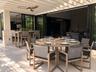 Covered patio featuring large-format stone flooring, wood-slat ceiling, integrated ceiling fan, and black-framed multi-panel sliding glass doors
