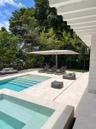 Outdoor space featuring a swimming pool with integrated spa, light-toned stone decking, wood-finish perimeter fencing, and a white pergola structure