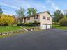 Split-level exterior featuring horizontal aluminum siding, stone veneer accents, an attached two-car garage, paved driveway and a stone retaining wall