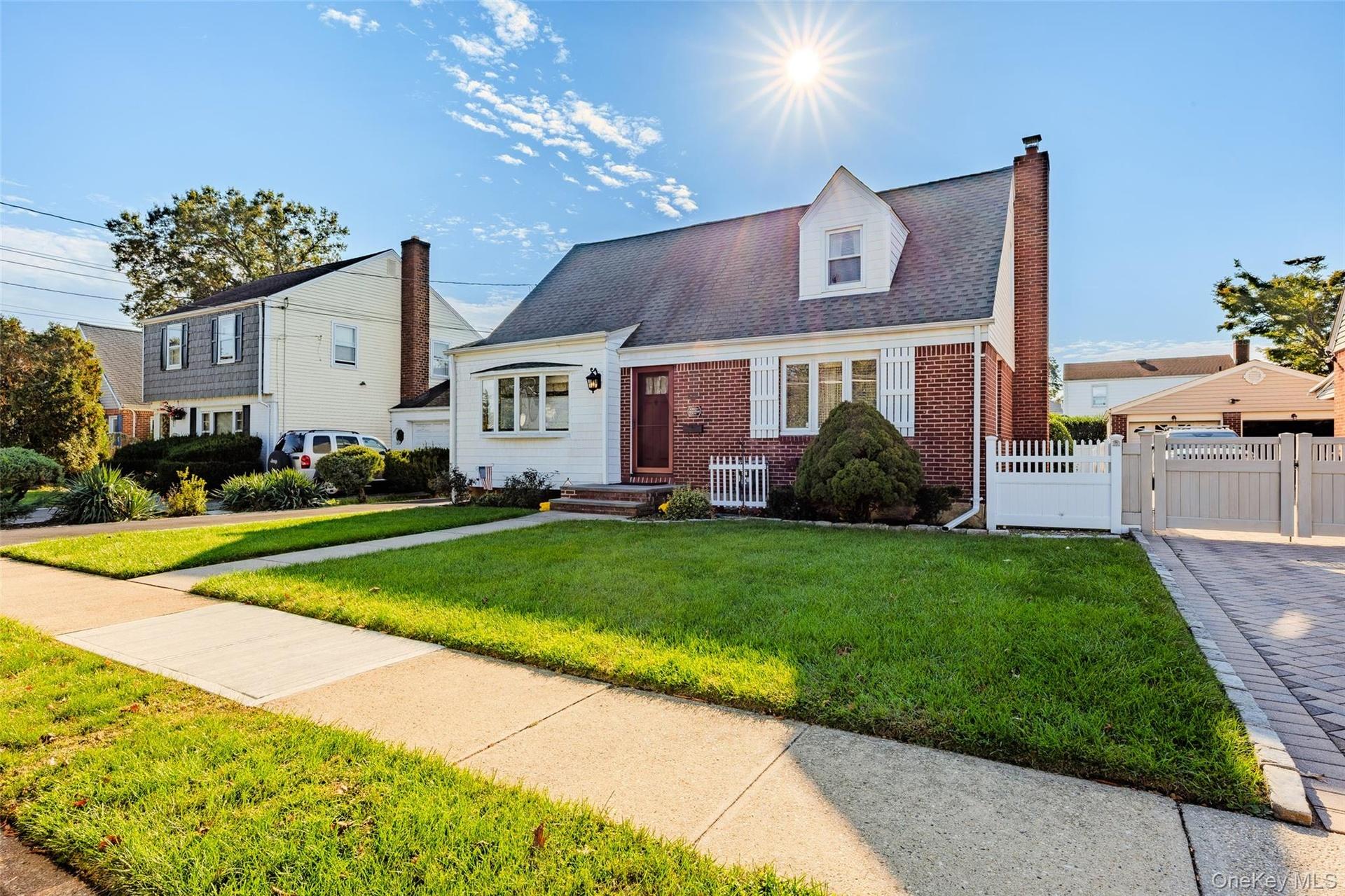 Cape Cod exterior featuring red brick and white siding, a front dormer window with privacy fencing