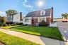 Cape Cod exterior featuring red brick and white siding, a front dormer window with privacy fencing