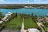Waterfront lot featuring direct canal access, expansive manicured lawn, mature palm trees, and a hard-surface tennis court