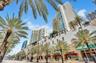 High-rise architectural exterior featuring multi-level balconies, ground-level retail storefronts with canvas awnings, and prominent palm tree landsca