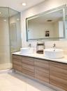 Floating vanity with wood-finish cabinetry, dual white vessel sinks, solid-surface countertop, and a large integrated LED-lit mirror, paired with a gl