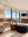 Floor-to-ceiling glass paneling with integrated balcony access, neutral stone-finish flooring, gold-tone modern circular chandelier, and custom built-