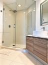 Floating wood-finish vanity with a white vessel sink, polished chrome faucet, glass-enclosed shower, and large-format tile flooring