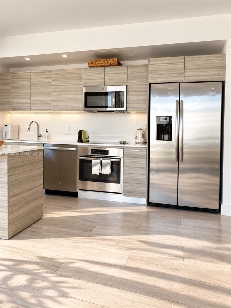 Kitchen featuring horizontal-grain wood-finish cabinetry, stainless steel appliances, solid-surface countertops, recessed ceiling lighting, and wood-f