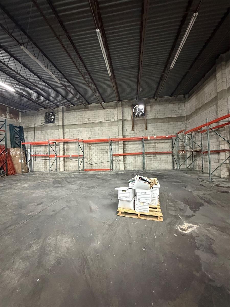 Industrial warehouse space featuring high ceilings with exposed metal trusses, concrete masonry unit walls, integrated wall-mounted exhaust fans, conc