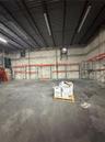 Industrial warehouse space featuring high ceilings with exposed metal trusses, concrete masonry unit walls, integrated wall-mounted exhaust fans, conc