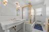 Pedestal sink with brass-finish faucet, gold-tone shower enclosure, white tile walls, and suspended lighting fixtures