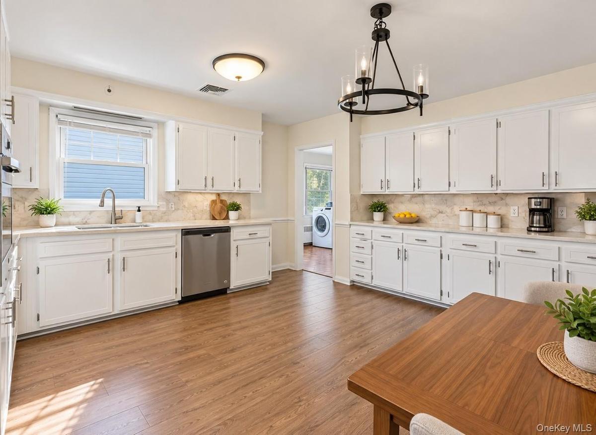 White cabinetry with brushed nickel hardware, light-toned countertops, stainless steel appliances, wood-finish flooring, and a contemporary chandelier