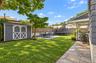 Expansive backyard featuring a manicured lawn, established trees, and a gray storage shed with white crossbuck doors