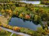 Expansive property grounds featuring a private pond, mature tree canopy, cleared open acreage, and several barns for horses