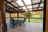 Covered outdoor screened deck featuring composite decking, exposed timber framing, and a translucent corrugated roof panel system