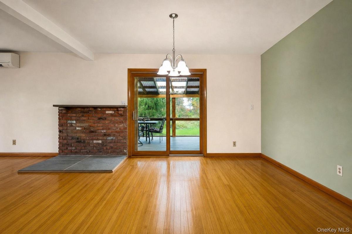 Hard wood flooring, exposed red brick fireplace hearth, sliding glass door to screened porch, multi-light chandelier, and accent wall