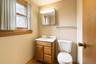 Wood-finish vanity with a white countertop and integrated sink, mirrored medicine cabinet, dual-handle faucet, and wooden window trim