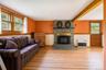 Living area featuring stone fireplace with wood stove insert and dual windows for view of front yard and pond, exposed ceiling beam.