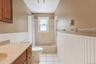 Bathroom featuring beadboard wainscoting, wood-finish cabinetry, a solid surface countertop with an integrated basin, tile flooring, and a tub-shower 