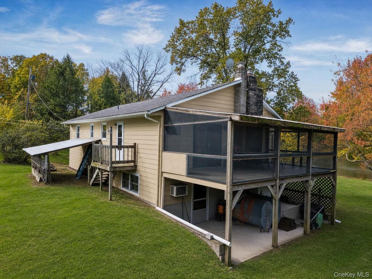 Exterior siding, elevated screened porch, raised wooden deck with railings, stone chimney, and covered lower-level patio