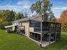 Exterior siding, elevated screened porch, raised wooden deck with railings, stone chimney, and covered lower-level patio