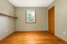 Hardwood flooring, natural light via a single window with wood-trim casing, built-in wall shelving, and a wood-finish closet door