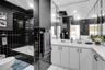 Bathroom featuring black square wall tiles, dual-sink vanity with white countertop, full-width mirror, and deep soaking tub with integrated shower