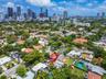 Aerial perspective of a property featuring a multi-section roofline, surrounding mature tree canopy, and metropolitan skyline backdrop