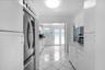 Kitchen featuring high-gloss white cabinetry, white stone-surface countertops, stainless steel refrigerator, tile flooring, and a glass-paneled exteri