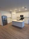 Kitchen featuring white cabinetry, an island with a light-toned countertop and sink, wood-finish flooring, and stainless steel appliances