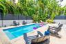 Rectangular in-ground pool with stone-tiled decking, enclosed by a two-tone privacy fence and mature perimeter landscaping