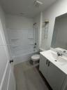 Bathroom featuring a white vanity cabinet with a stone countertop, integrated sink, large wall-mounted mirror, and a tub-shower combination with built
