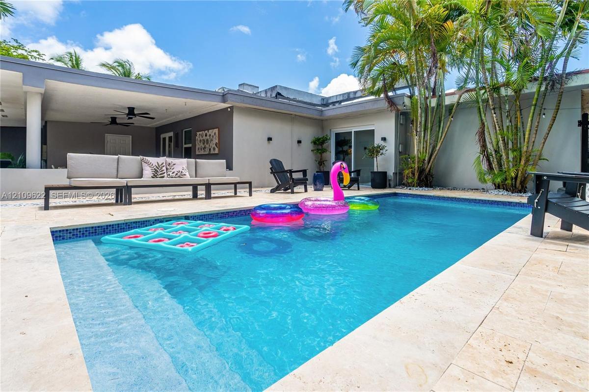 In-ground swimming pool with tile surround, covered patio with recessed ceiling fans, and natural stone-finish decking