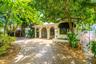 Exterior facade featuring arched entryways with decorative iron security grilles, a barrel-tile roofline, concrete driveway, and mature landscaping
