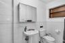 Bathroom featuring white tile wall cladding, wall-mounted three-panel mirrored medicine cabinet, porcelain pedestal sink, and fixed-pane window